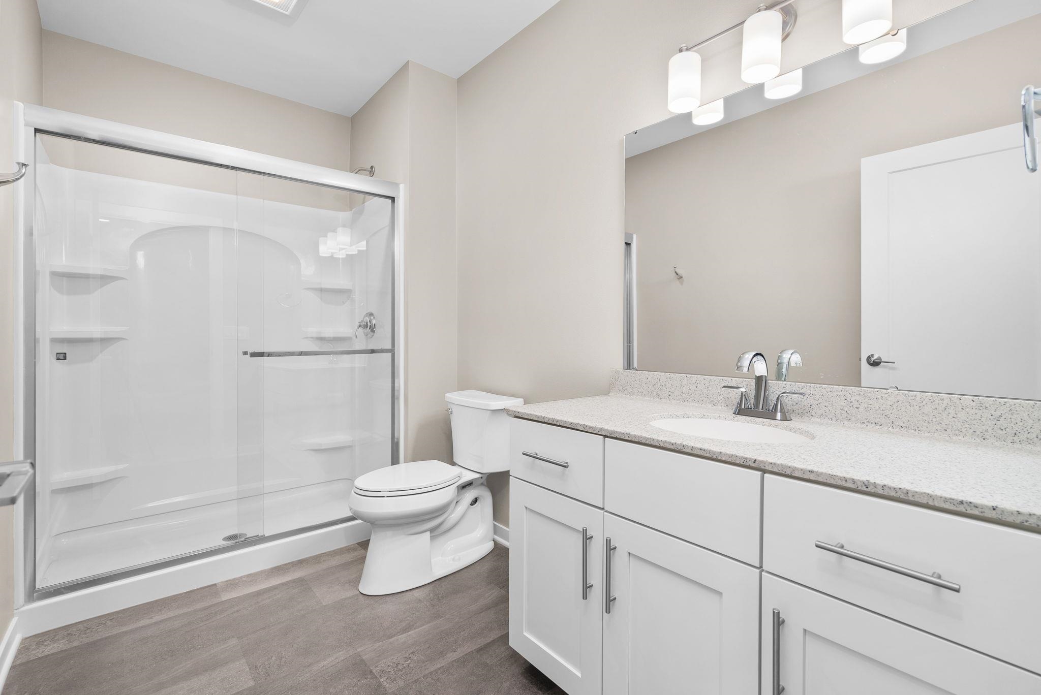 Bathroom with a glass-enclosed shower, white vanity, speckled countertop, and large mirror.