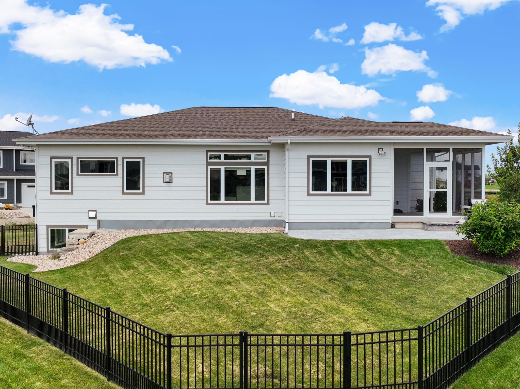 House rear exterior with a fenced green lawn, black metal fencing, and a small paved patio.