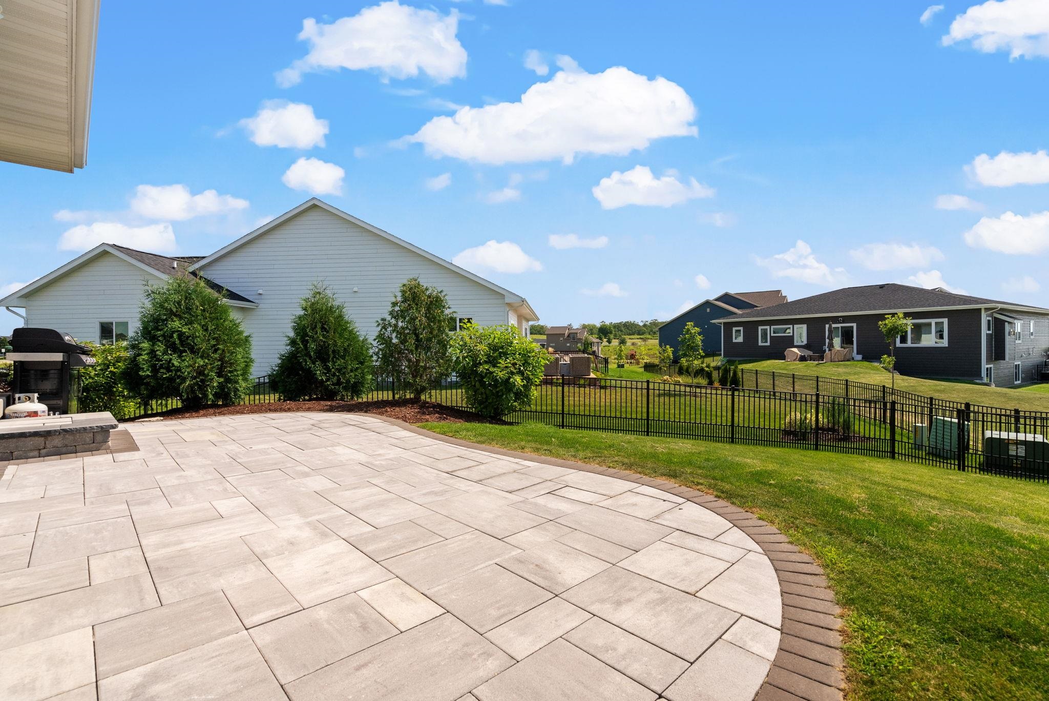 Backyard patio with a broad curved paver terrace, black metal fence, and landscaped lawn.