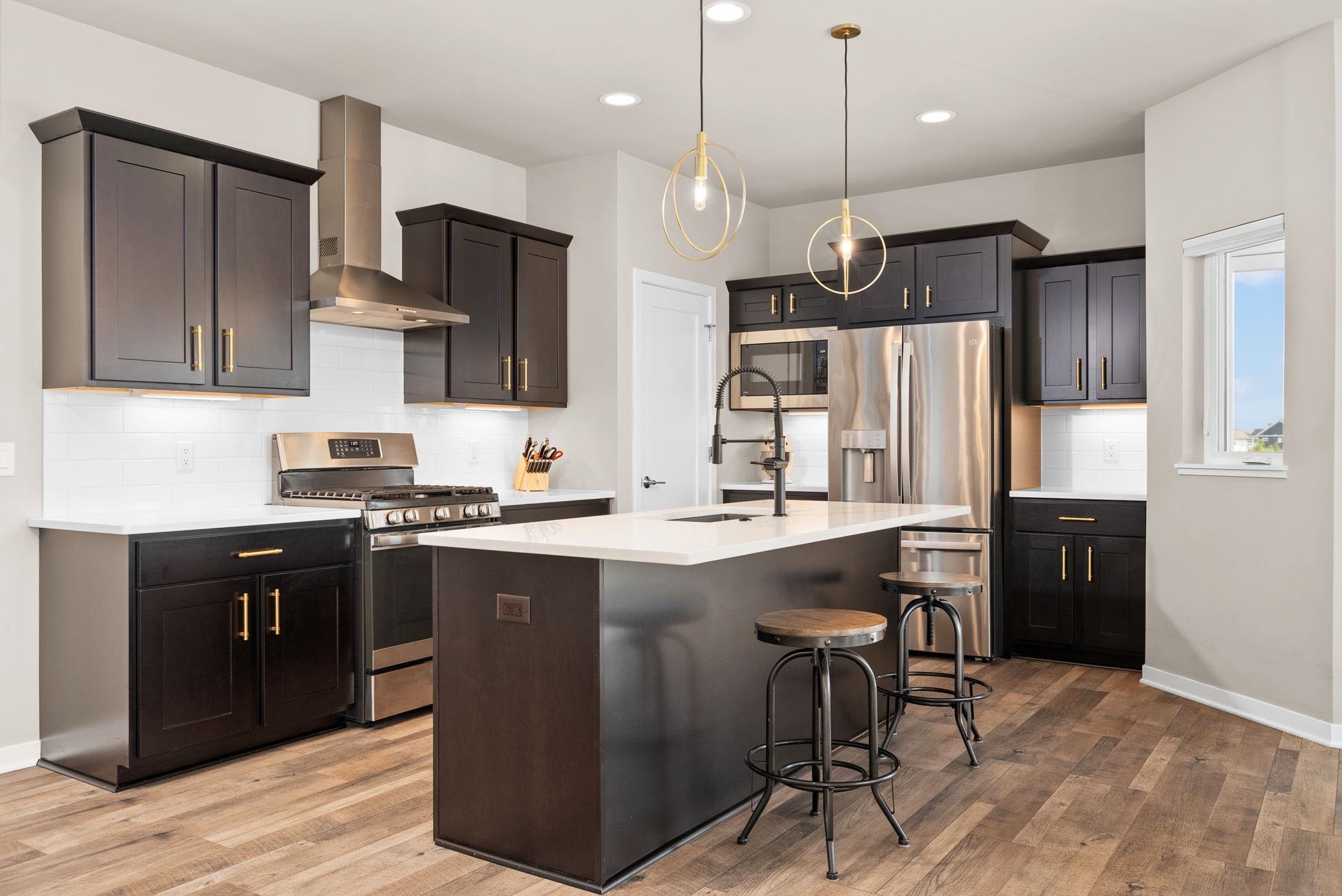 Modern kitchen with dark cabinets, stainless steel appliances, and a large island with stools.