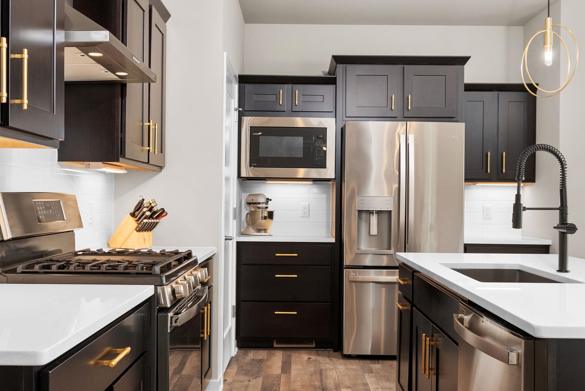 Modern kitchen with dark cabinets, brass hardware, stainless appliances, and a white island with sink.