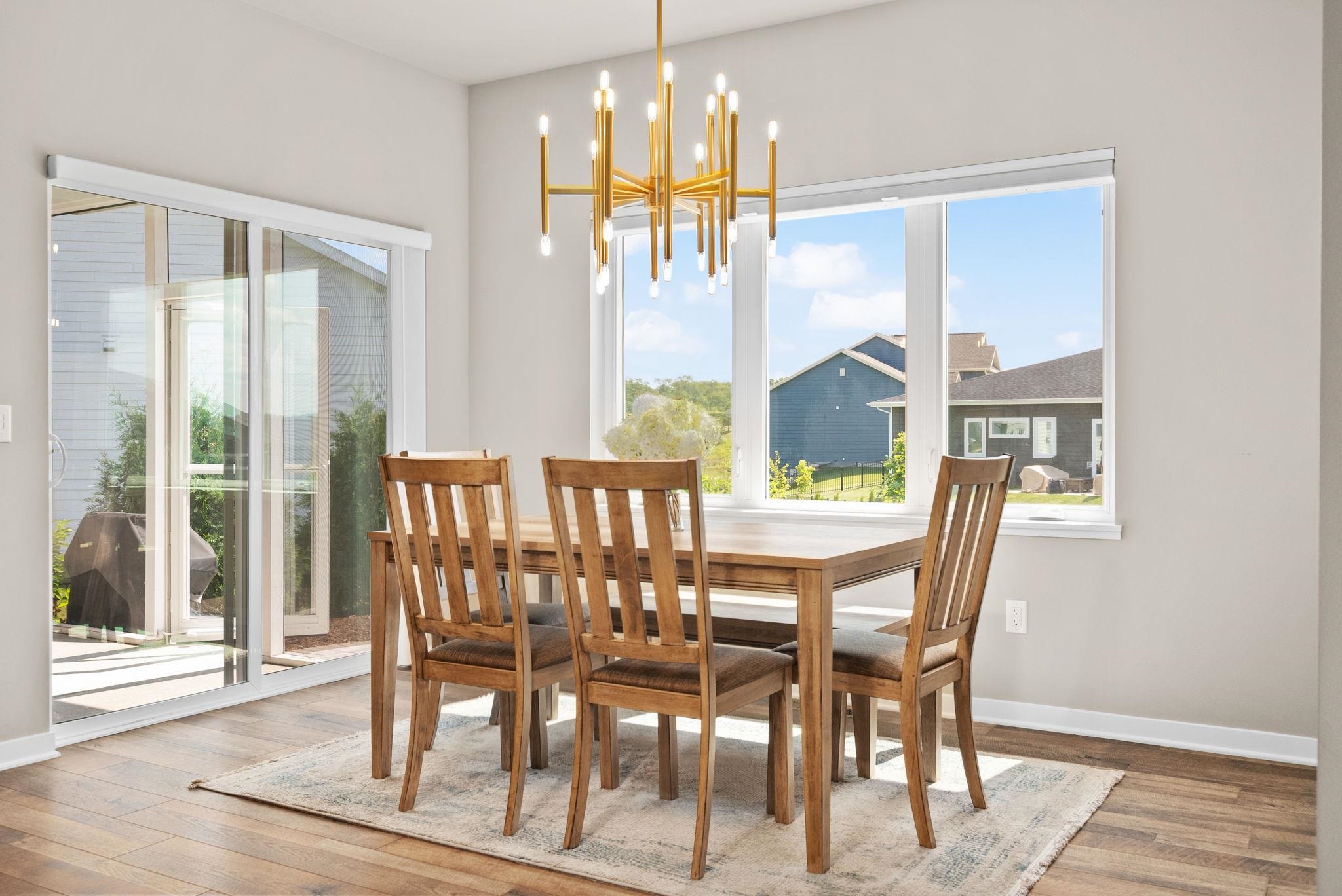 Dining room with a wooden table, gold chandelier, and large windows overlooking neighboring homes.