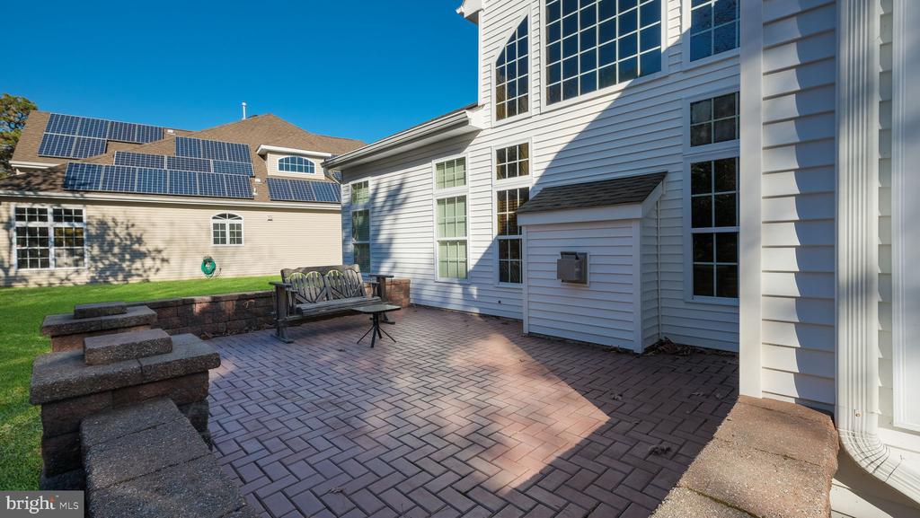 White-sided home with a brick patio, stone seating wall, and a wooden bench.