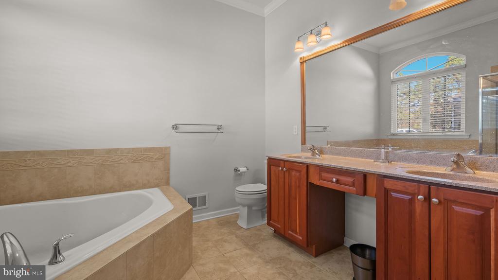 Bathroom with a tiled soaking tub, wood double vanity, large mirror, and arched window.