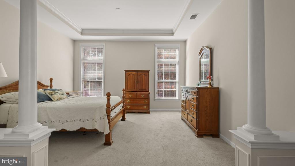 Furnished bedroom with a four-poster wooden bed, matching dressers, and white columns.
