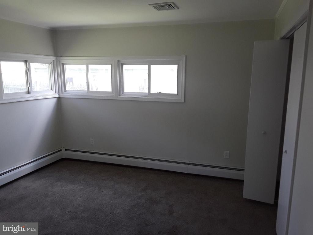 Empty carpeted room with windows along two walls and baseboard heaters.