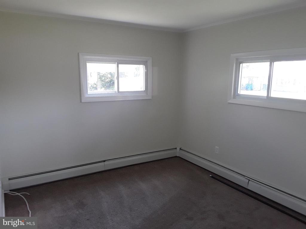 Vacant bedroom with gray carpet, two windows, and baseboard heating.