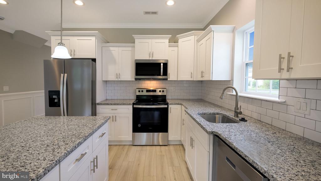 Renovated kitchen with white cabinets, granite counters, stainless steel appliances, and a large island.