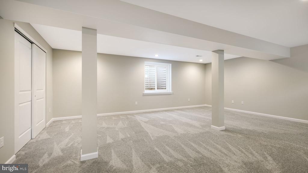 Finished basement with gray carpet, two support columns, and a small shuttered window.