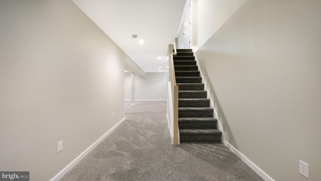 Empty carpeted basement with a staircase and open finished area beyond.