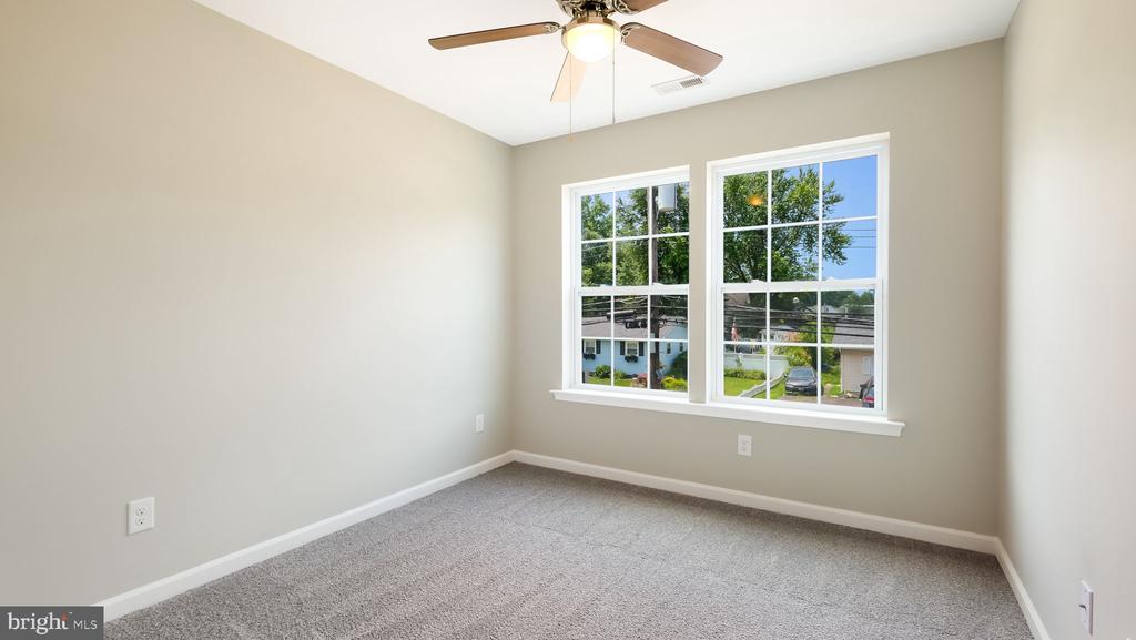 Empty bedroom with gray carpet, a ceiling fan, and two large windows.