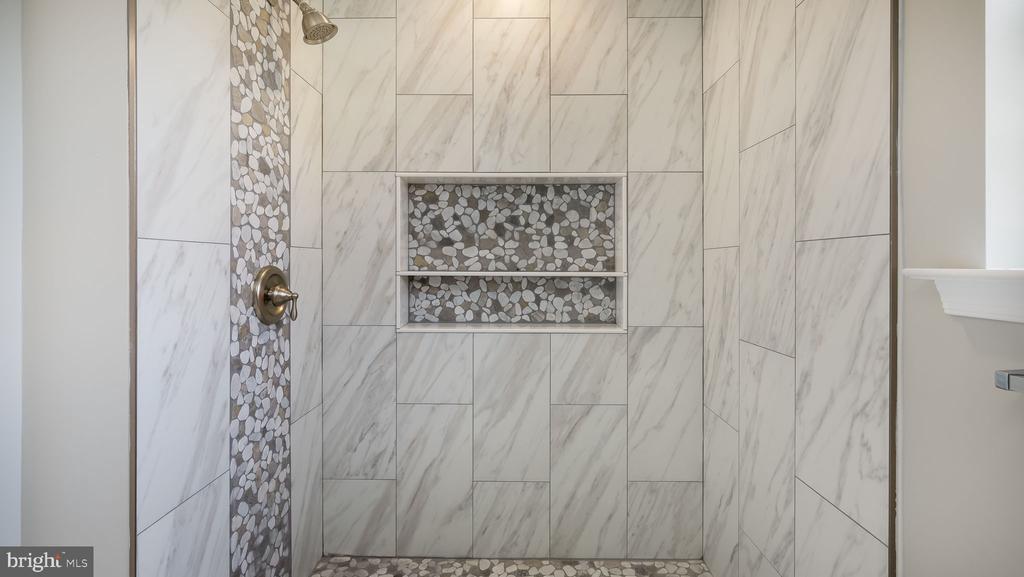 Walk-in shower with marble-look tile, pebble mosaic accents, and a recessed double shelf.