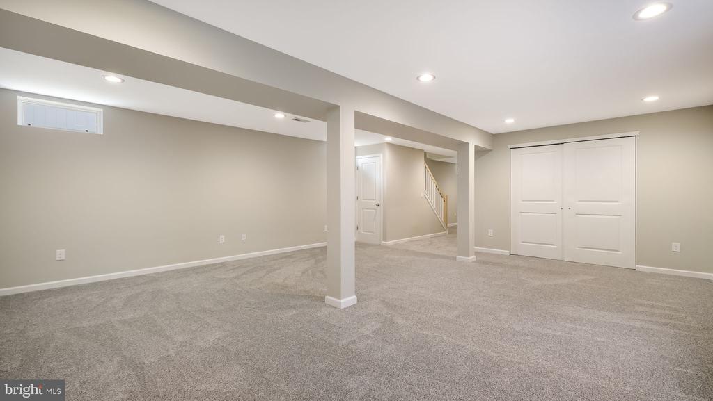Finished basement with beige carpeting, support columns, and white double closet doors.