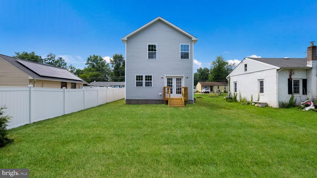 Rear of a gray two-story house with a small wooden deck and broad fenced lawn.