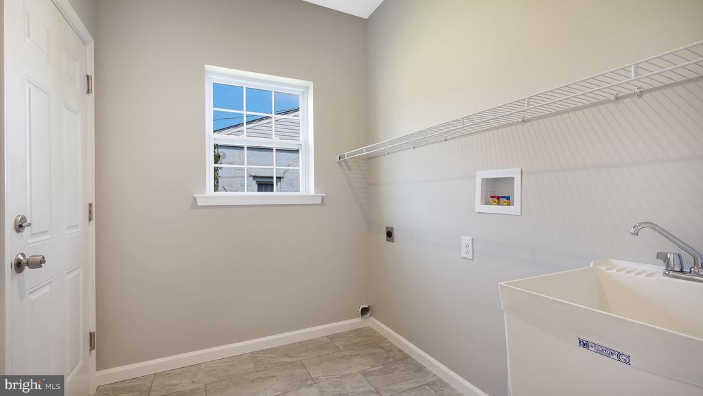 Empty laundry room with a deep utility sink, wire shelving, and tiled floor.