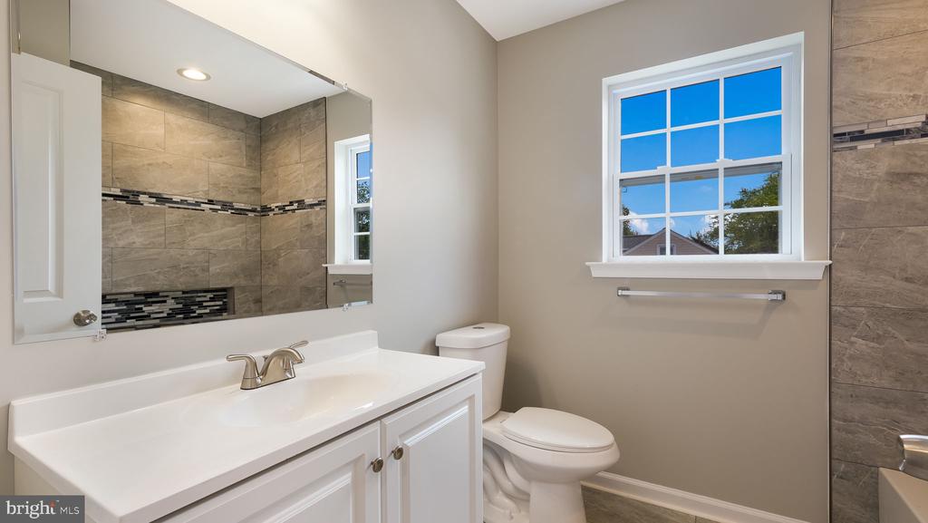 Bathroom with a white vanity, large window, and tiled shower with mosaic accents.