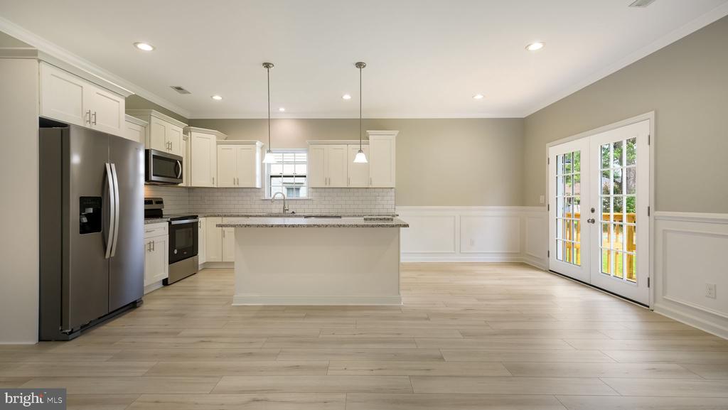 Unfurnished kitchen with a large island, stainless steel appliances, and French doors to a deck.