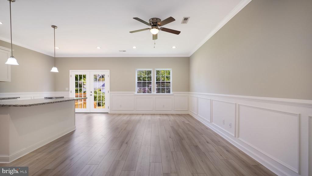 Open living and dining area with wood floors, white wainscoting, and French doors to a deck.