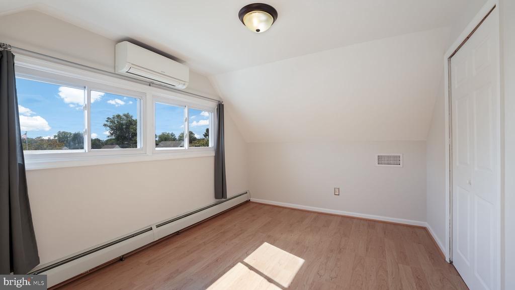 Empty room with light wood floors, sloped ceiling, wide windows, and a wall-mounted air conditioner.