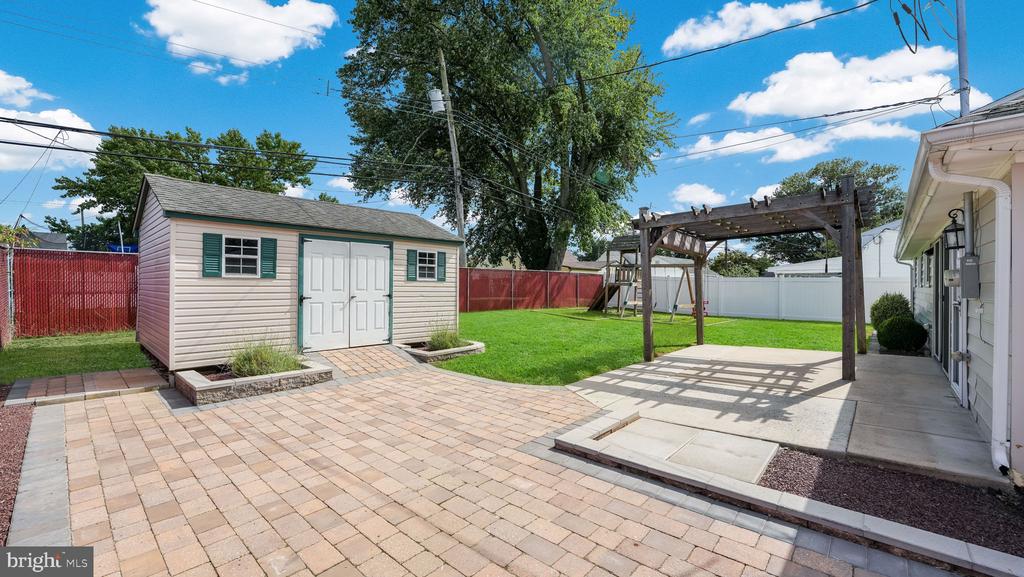 Backyard with a detached shed, wooden pergola, paved patio, lawn, and fenced yard.