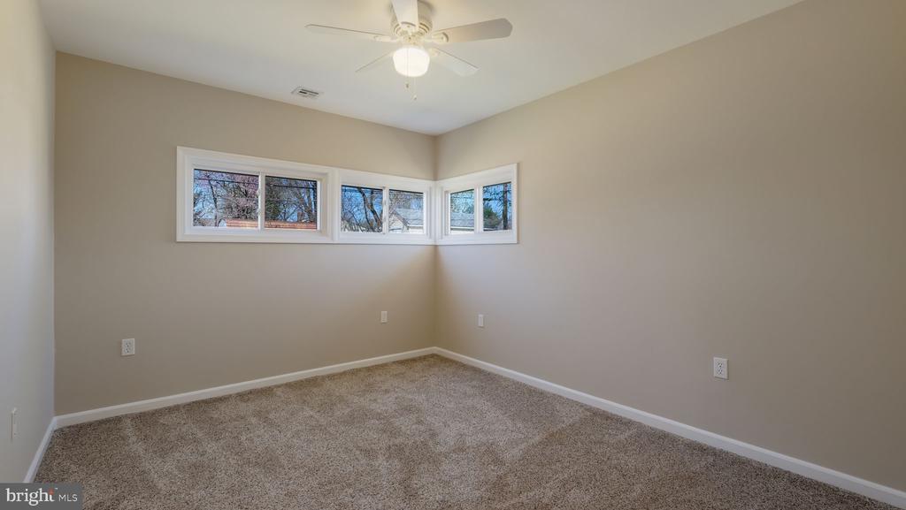 Vacant bedroom with wall-to-wall carpet, a ceiling fan, and high corner windows.