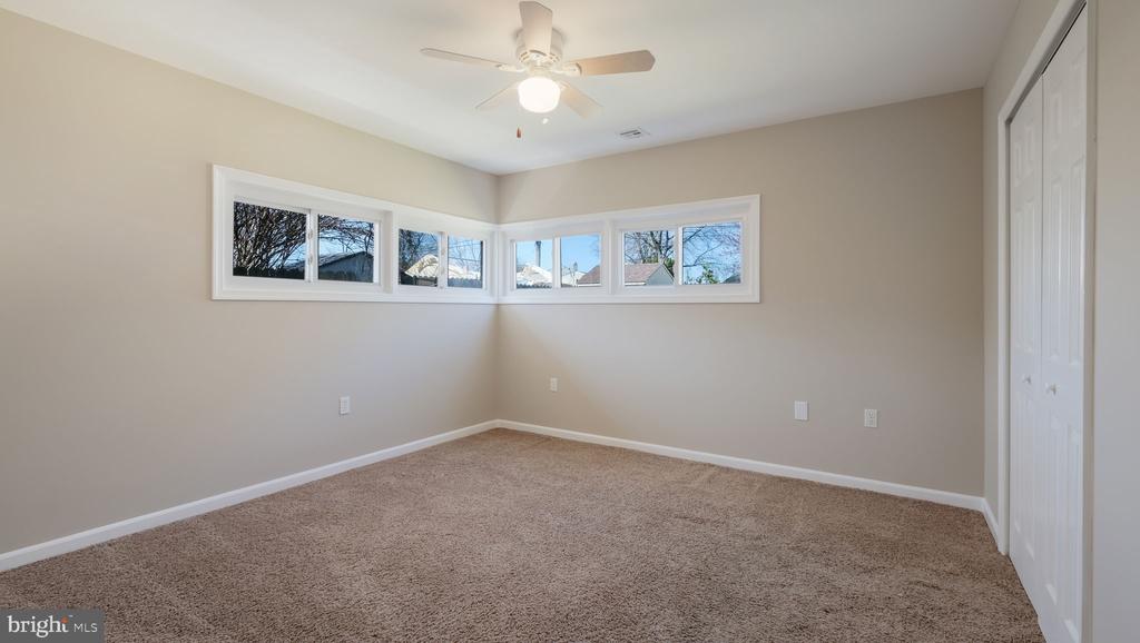 Vacant bedroom with corner windows, brown carpet, a ceiling fan, and white closet doors.