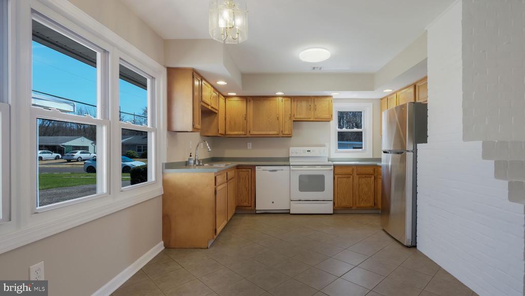 Kitchen with honey-colored cabinets, white appliances, and large windows overlooking the street.