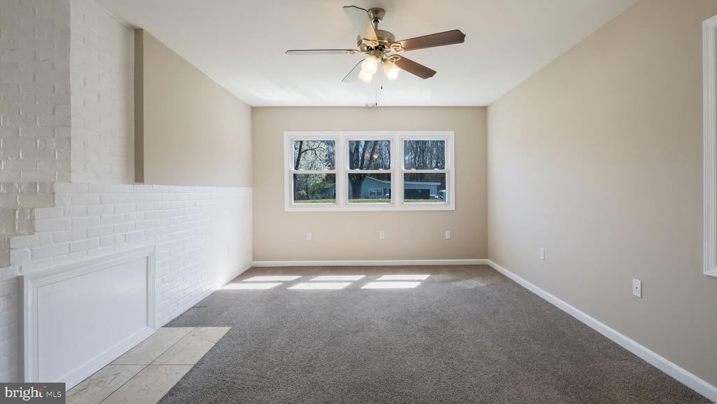 Vacant living room with gray carpet, a white brick fireplace, and three windows.