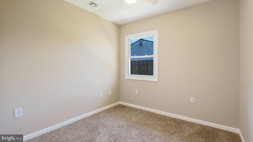 Empty beige room with tan carpeting, white trim, and a window overlooking a fence.