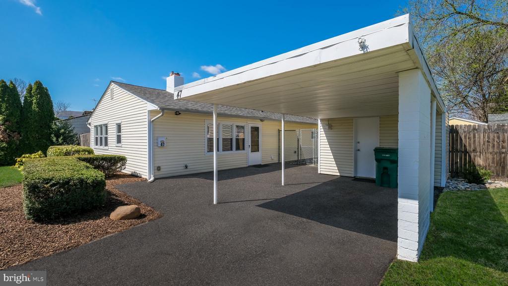 Single-story home with a broad white carport, paved driveway, and landscaped shrubs.