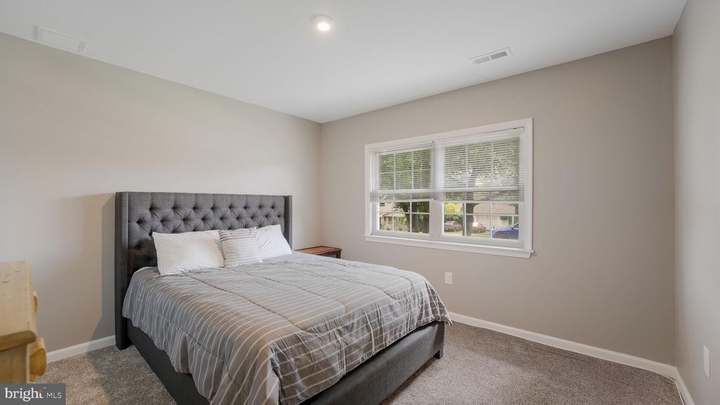 Bedroom with a gray tufted bed and a window overlooking the street.