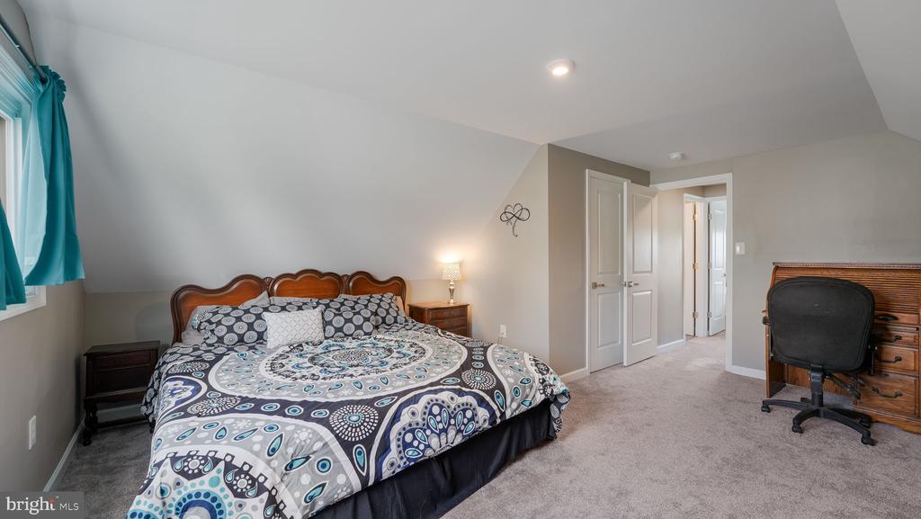 Attic bedroom with patterned bedding, teal curtains, and a desk beneath a sloped ceiling.