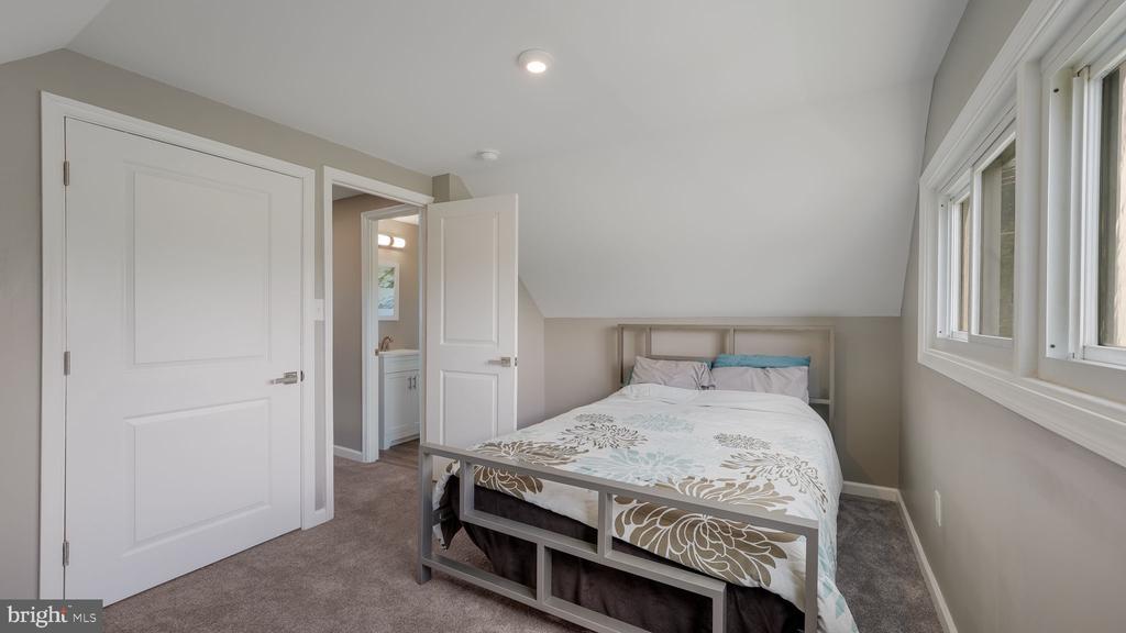 Furnished bedroom with a sloped ceiling, large windows, and an open doorway to the bathroom.