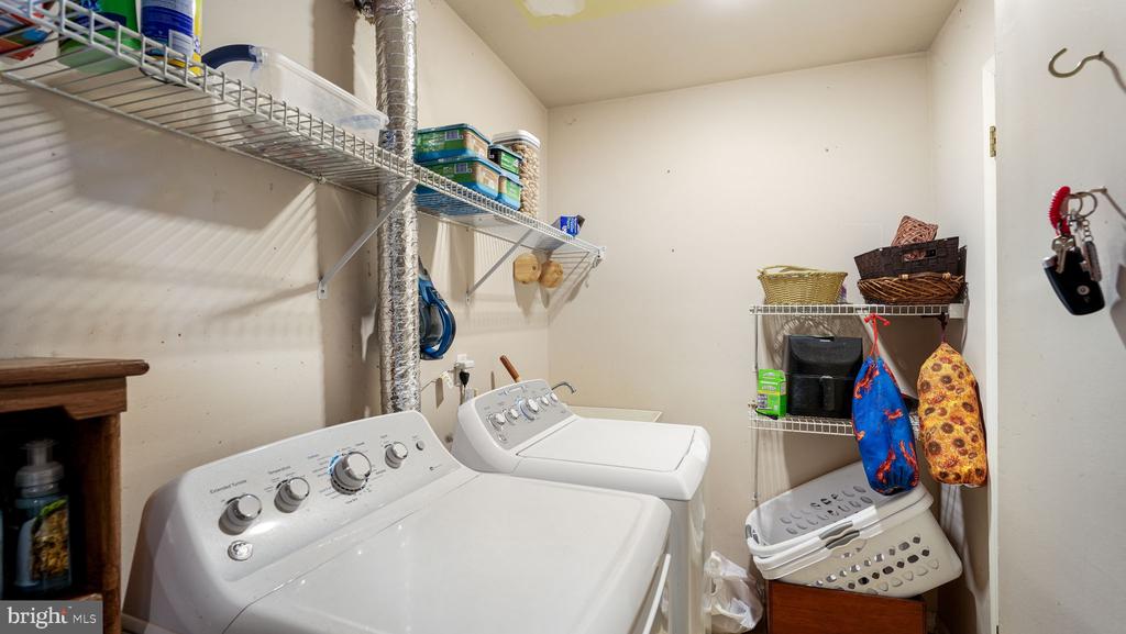 Laundry room with a top-loading washer and dryer, wire shelves, and hanging bags.