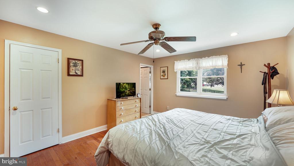 Bedroom with a large bed, hardwood floors, ceiling fan, and window overlooking trees.