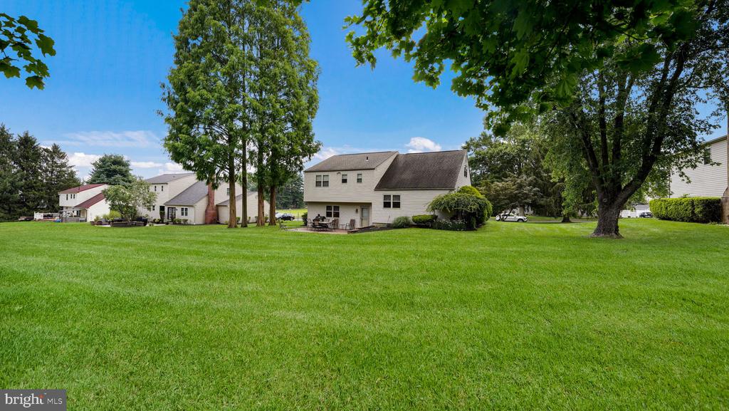 Two-story light-sided house behind a broad lawn, with a small patio and mature trees.
