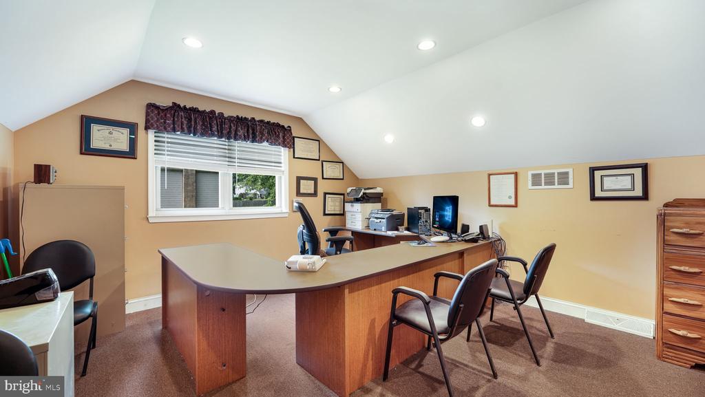 Home office with an L-shaped desk, multiple chairs, and a window beneath a sloped ceiling.