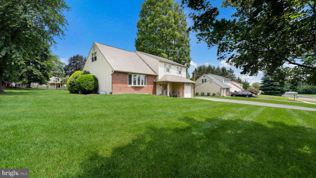 Two-story brick-and-siding home beyond a broad lawn, with mature trees and neighboring houses.