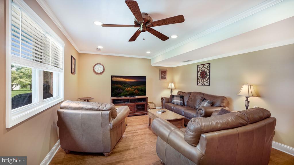 Living room with brown leather sofas, a ceiling fan, and a large window with white blinds.