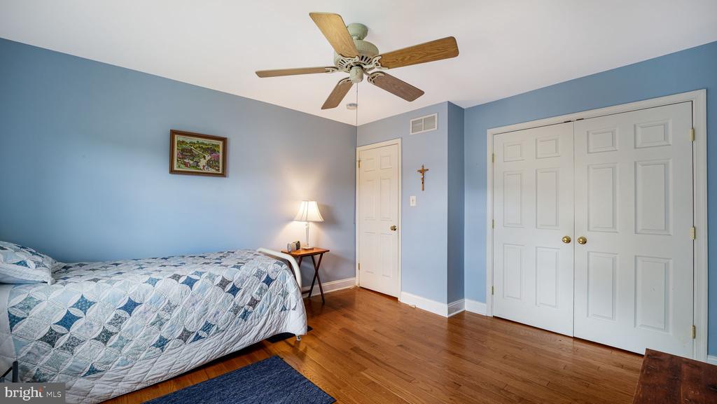 Bedroom with blue walls, a blue-and-white quilt, hardwood floors, and white closet doors.