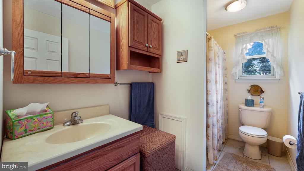 Bathroom with a wood vanity, mirrored medicine cabinet, and toilet beneath a curtained window.