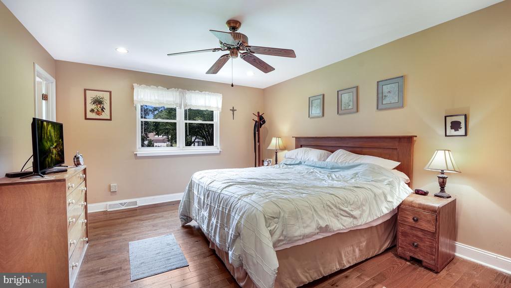Bedroom with a large bed, hardwood floors, ceiling fan, and window with sheer curtains.