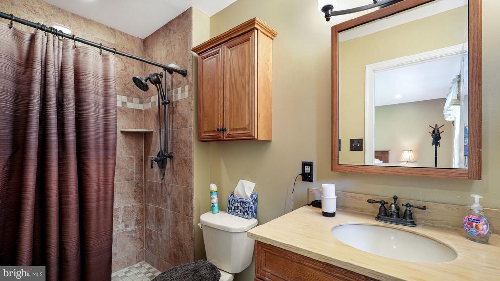 Bathroom with tiled shower, brown curtain, wooden vanity, cream countertop, and large framed mirror.