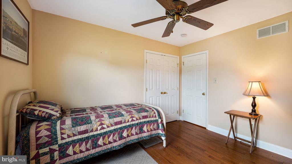 Bedroom with a colorful patchwork quilt, hardwood floors, ceiling fan, and lit bedside lamp.