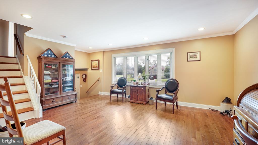 Furnished living room with hardwood floors, staircase, display cabinet, and chairs beside a wide window.