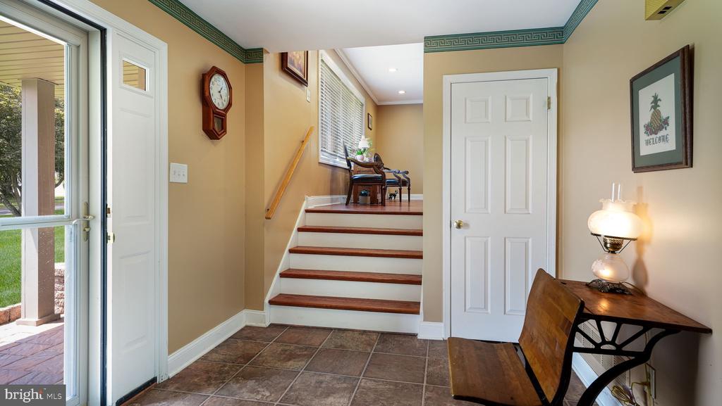 Entry foyer with tiled floor, wood-tread staircase, and a small table and chair.
