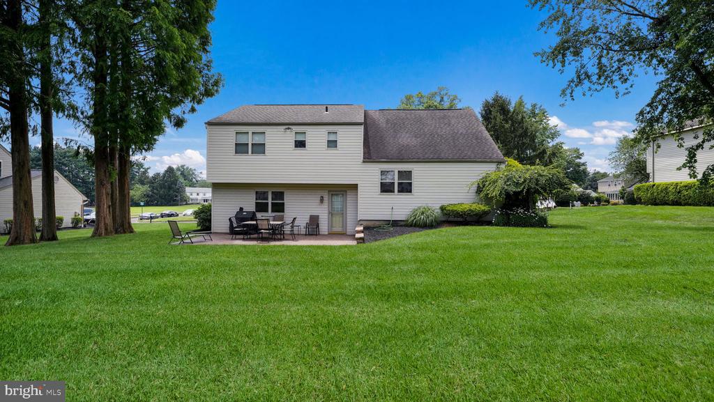 Rear exterior of a two-story home with a broad lawn, patio seating, and mature trees.