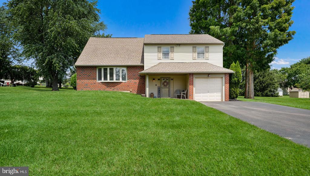 Two-story brick and siding house with a one-car garage, broad lawn, and mature trees.