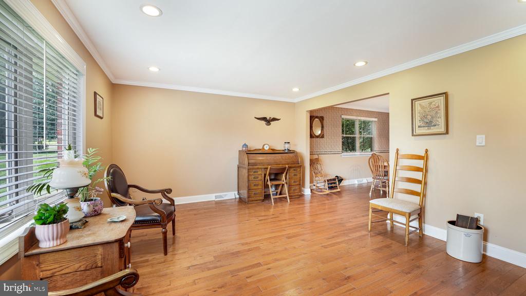 Living room with hardwood floors, a large blinded window, wooden desk, and chairs.