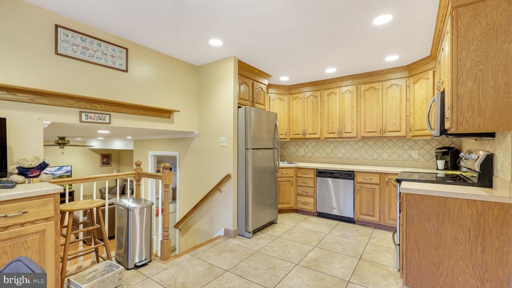 Kitchen with honey-colored wood cabinets, stainless steel appliances, and tile flooring.